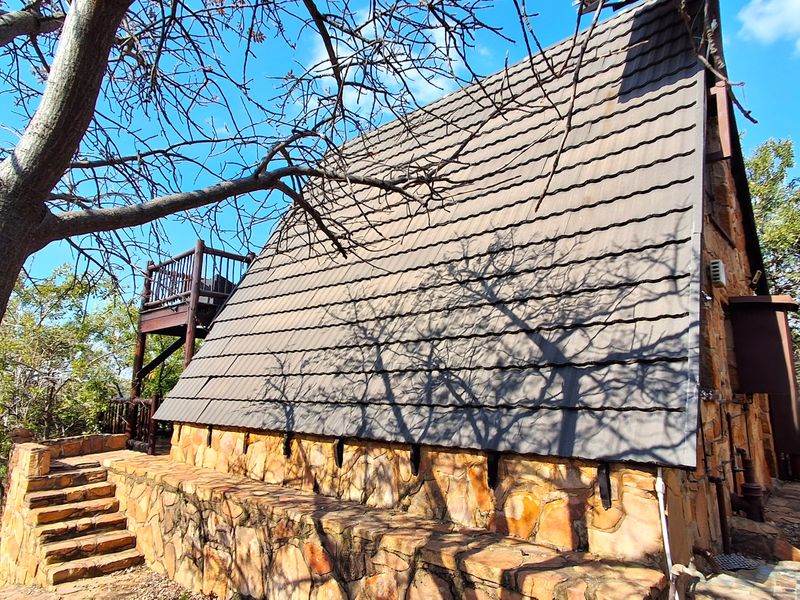 Rear view of a rustic townhouse featuring stone cladding, a steep tiled roof, and an elevated wooden balcony set within a natural landscape.