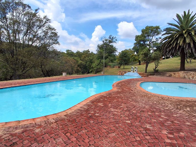 A spacious outdoor swimming pool area featuring a paved deck, stone retaining walls, and landscaped surroundings in a tranquil setting.