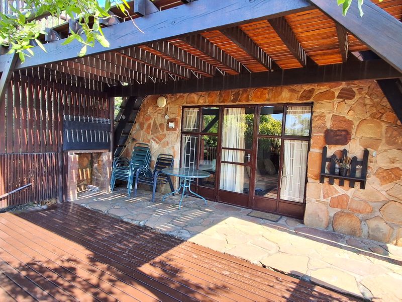 Covered outdoor patio featuring a timber deck, stone-clad wall, and built-in braai, providing a rustic space for outdoor entertaining.