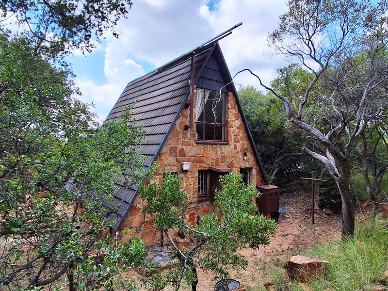 A rustic A-frame townhouse featuring stone cladding and a tiled roof, nestled within a natural, wooded environment.