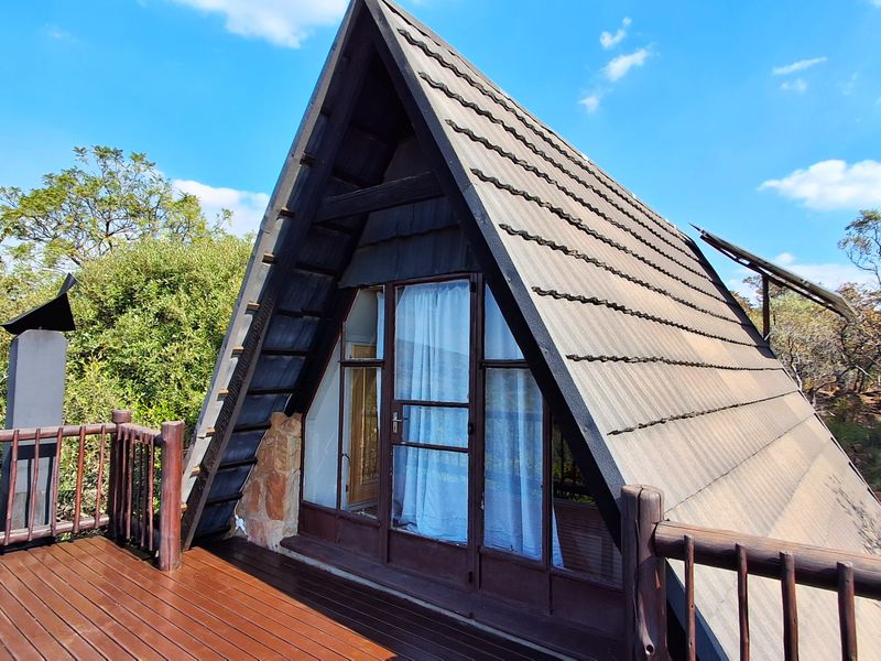 A-frame townhouse exterior featuring a timber deck, stone masonry accents, and large glass doors, set within a natural, wooded environment.