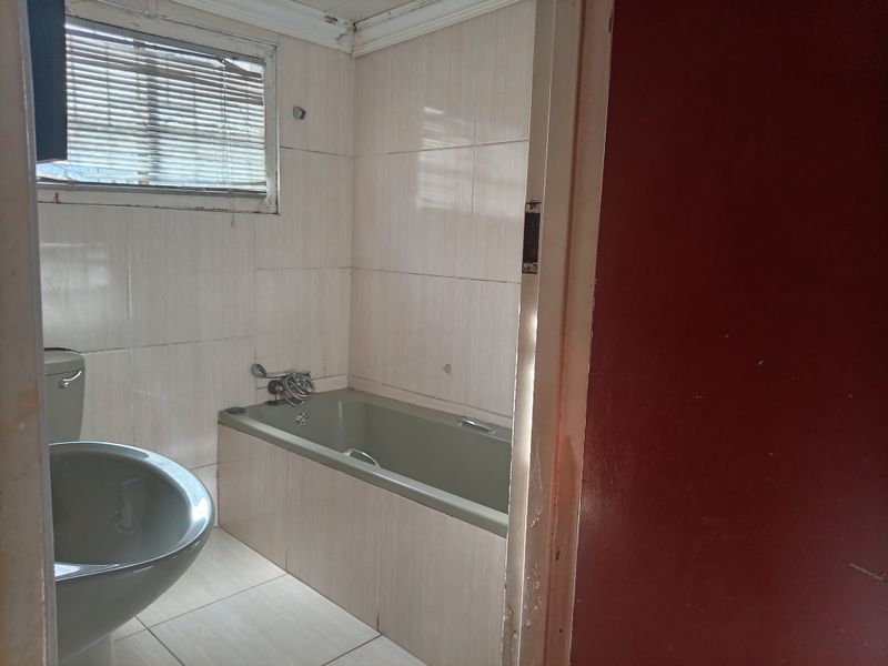 A dated bathroom featuring a built-in bathtub, toilet, and full-height wall tiling, requiring cosmetic updates to modernize the space.