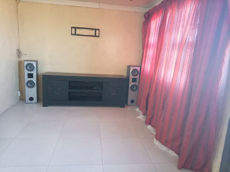 A living room featuring tiled flooring and coving, with a wall-mounted television bracket. The space requires cosmetic updates to improve its overall condition.