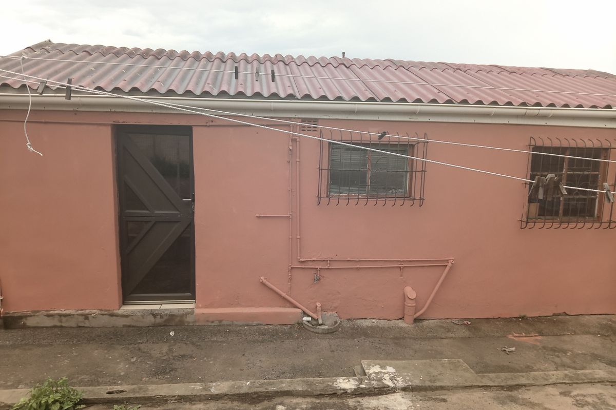 Rear exterior view of the property featuring a corrugated roof, security bars on windows, and exposed external plumbing along the painted wall.