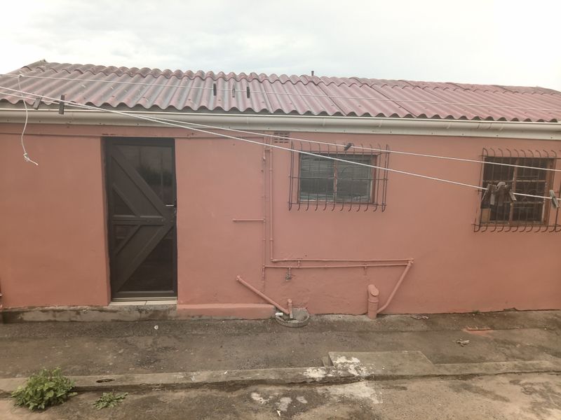 Rear exterior view of the property featuring a corrugated roof, security bars on windows, and exposed external plumbing along the painted wall.