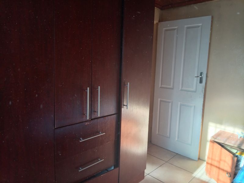 Bedroom featuring built-in dark wood cupboards and tiled flooring, requiring minor cosmetic updates to the walls and door frame.