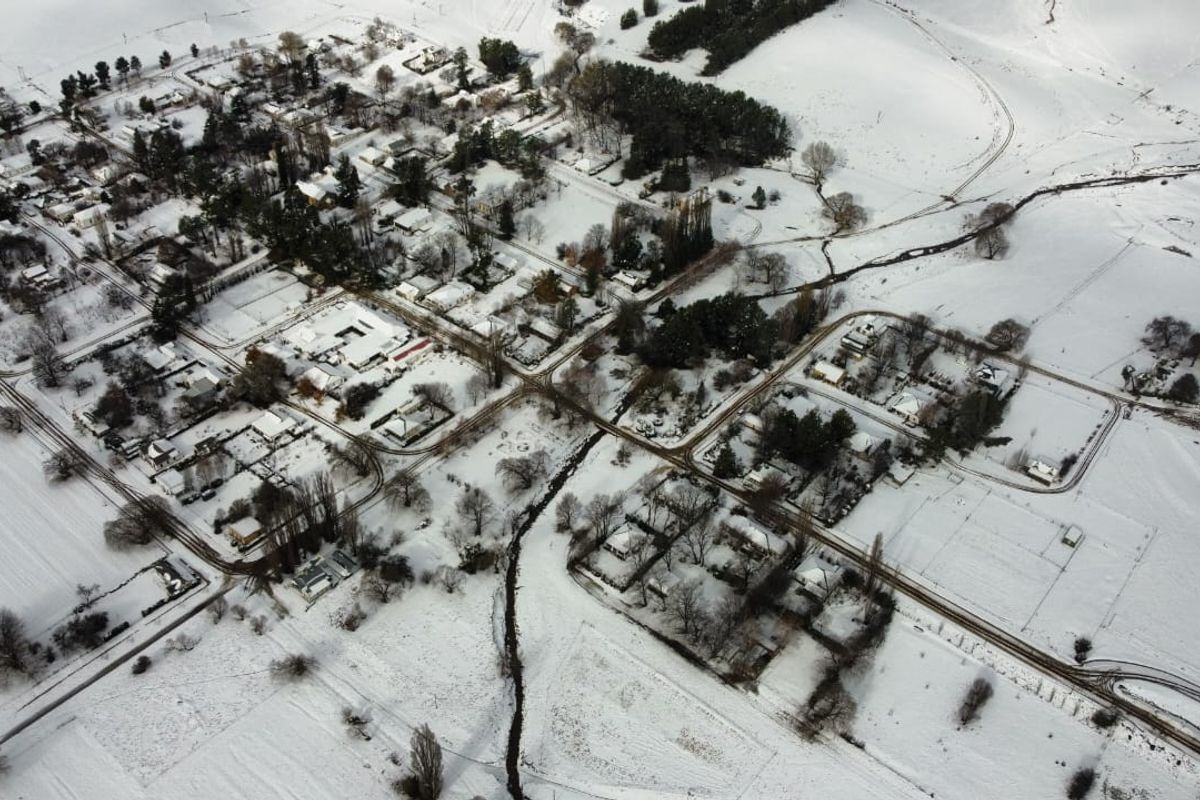 An aerial view of a residential area covered in snow, showcasing the layout of the neighborhood and surrounding landscape.