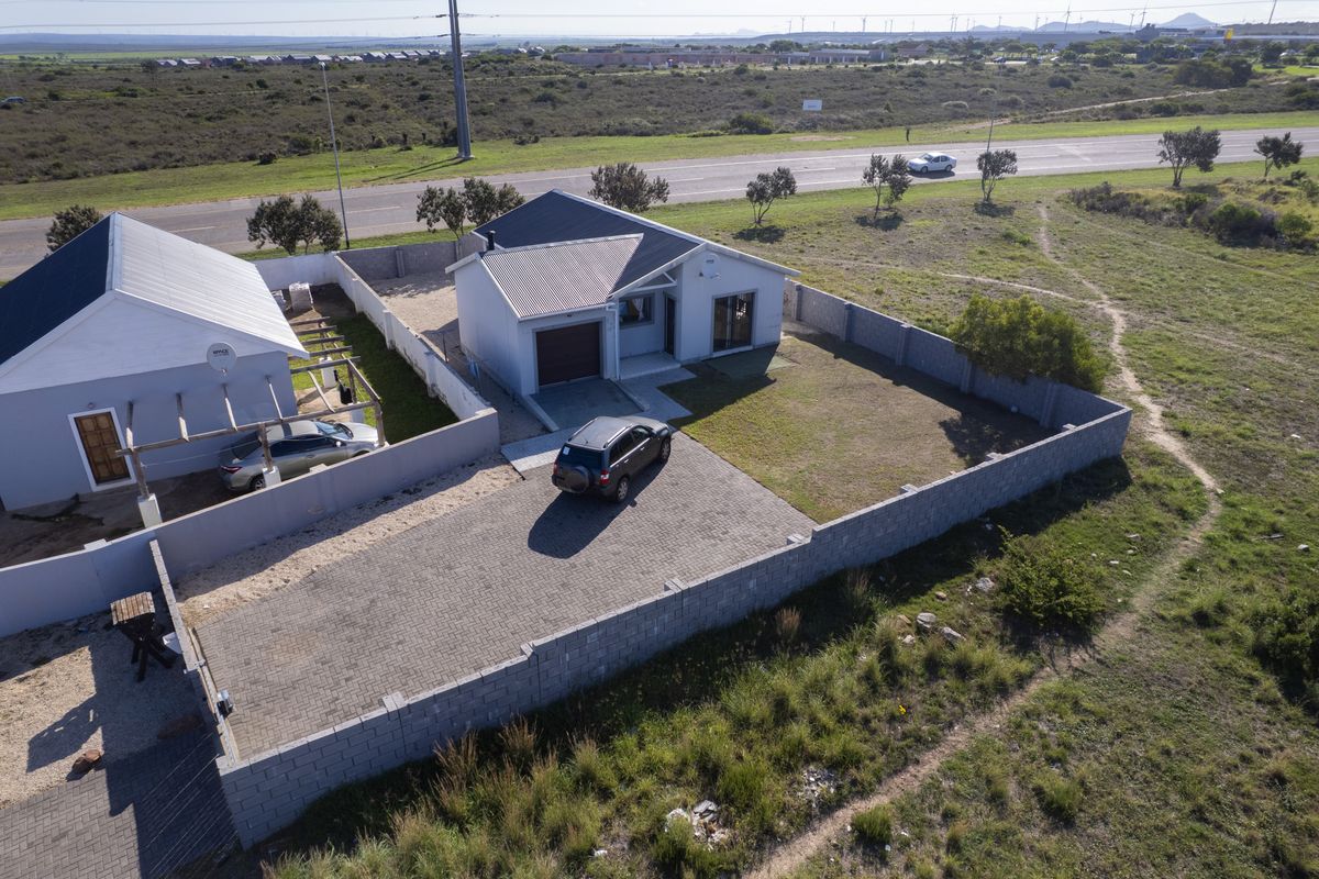 Aerial view of a detached residential property featuring a paved driveway, perimeter walling, and a corrugated metal roof.