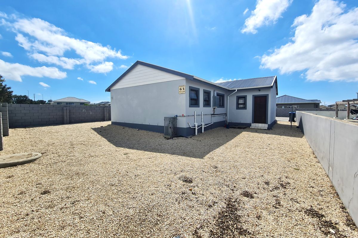 Rear view of the property featuring a low-maintenance gravel yard, concrete block boundary walls, and external building infrastructure.