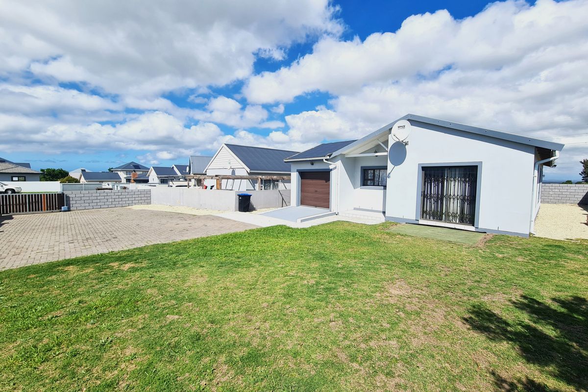 Rear view of the property featuring a paved driveway, garage access, and a private garden area with boundary walling.