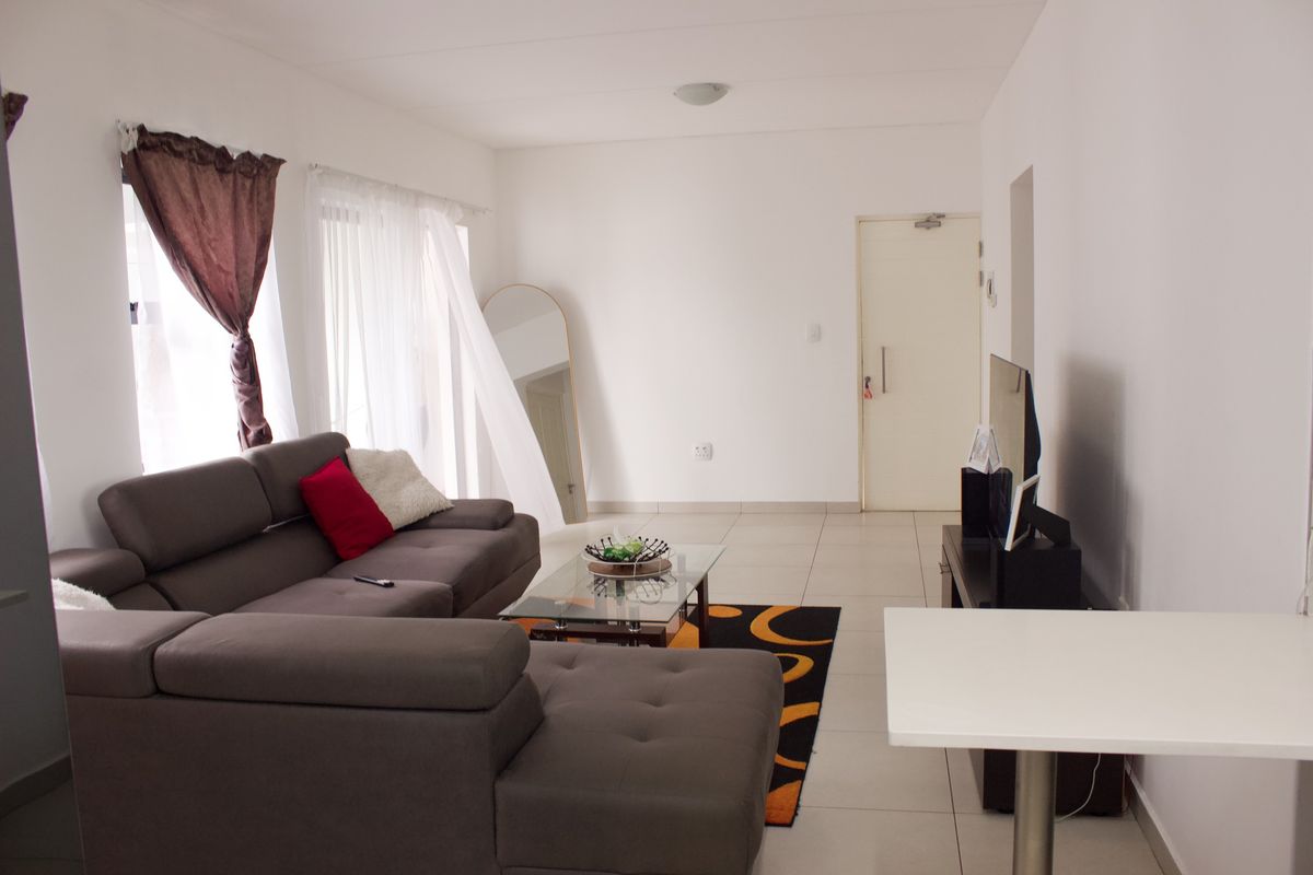 A bright, open-plan living area featuring neutral tiled flooring and clean white walls, providing a versatile space for relaxation and entertainment.