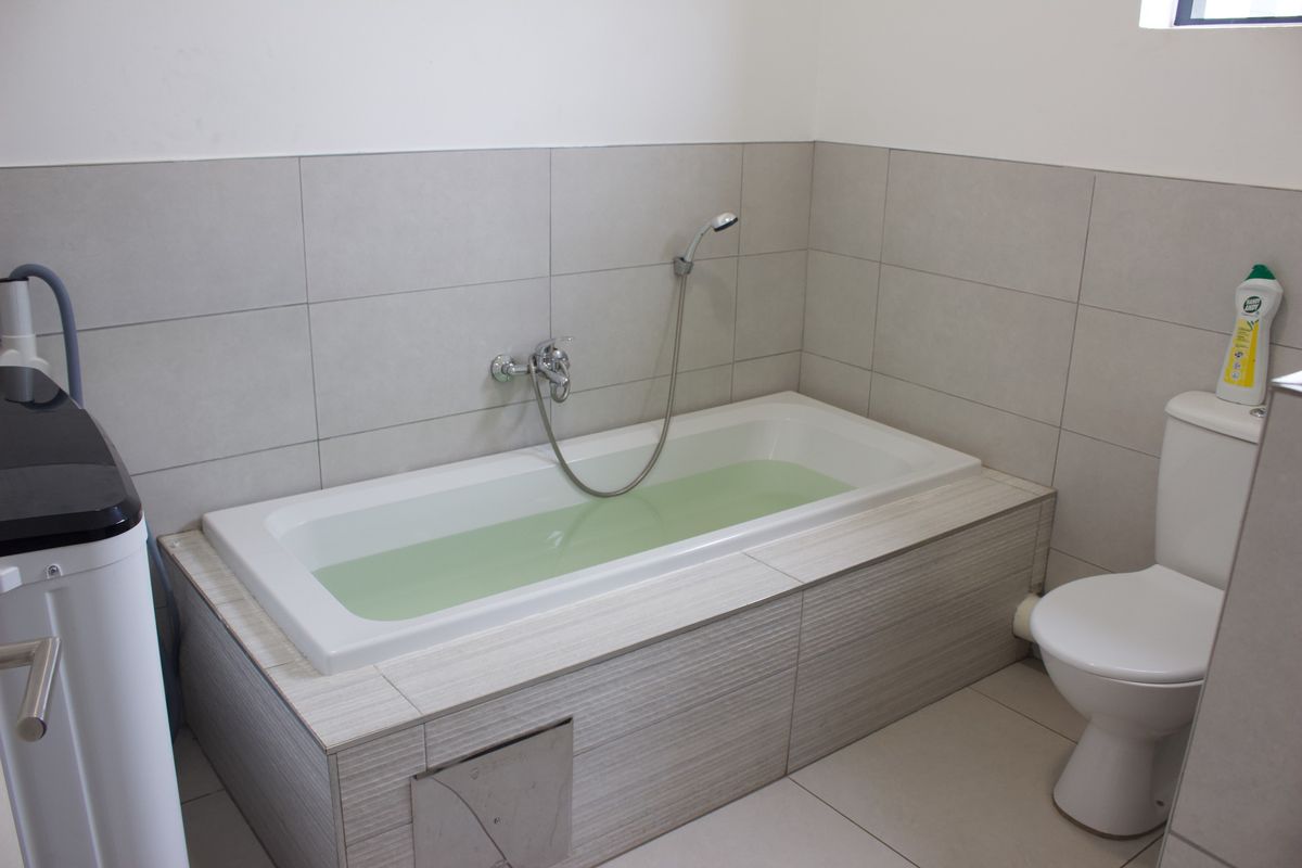 A functional bathroom featuring a built-in bathtub with a handheld shower attachment, tiled surround, and a standard toilet.