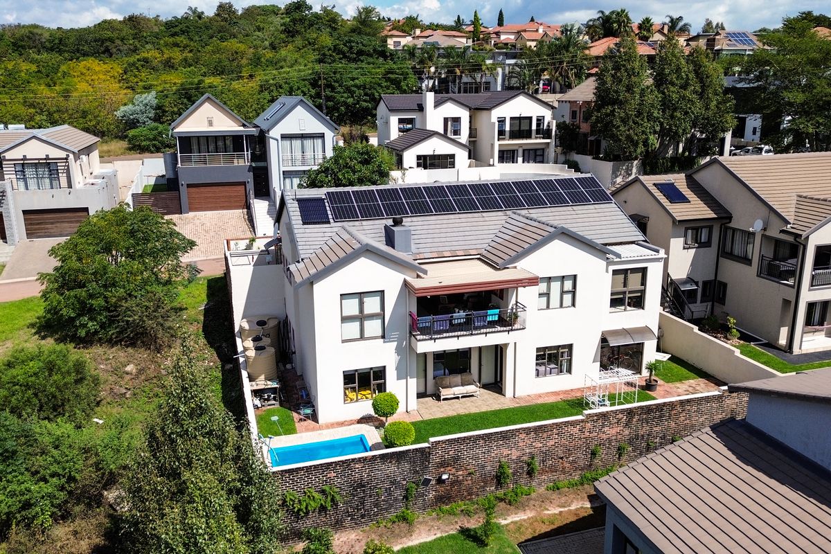 Aerial view of a residential property featuring a tiled roof with solar panels, a private swimming pool, a rear patio, and a landscaped garden.