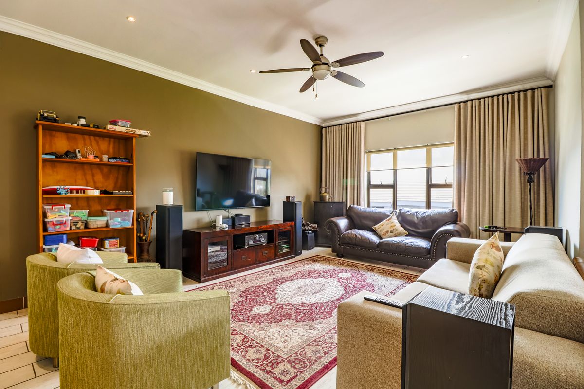 A comfortable living room featuring recessed ceiling lighting, a central ceiling fan, and large windows with floor-to-ceiling curtains.