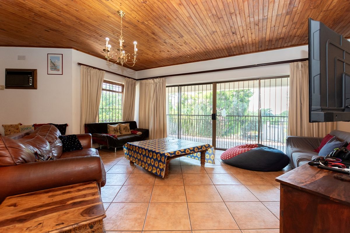 Spacious living room featuring a vaulted timber-clad ceiling, ceramic floor tiles, and large sliding glass doors opening to a balcony with security bars.