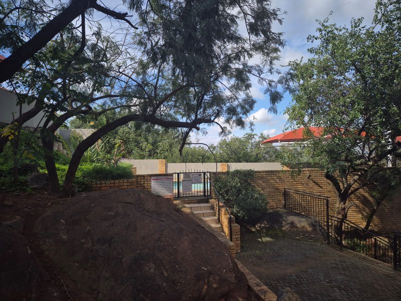 Outdoor pool area access featuring brick boundary walls, paved pathways, and stone steps leading to a secure gated entrance.