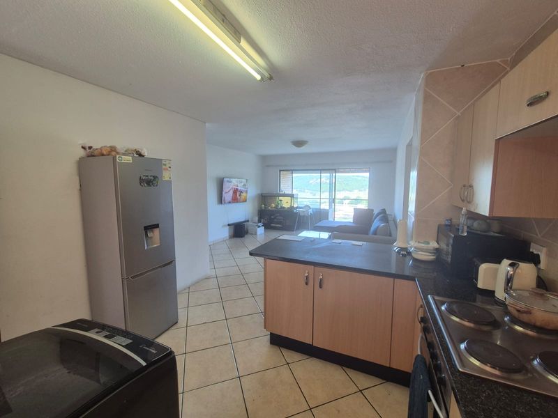 Open-plan living and kitchen area featuring tiled flooring, built-in cabinetry with granite countertops, and a sliding door leading to a balcony with views.