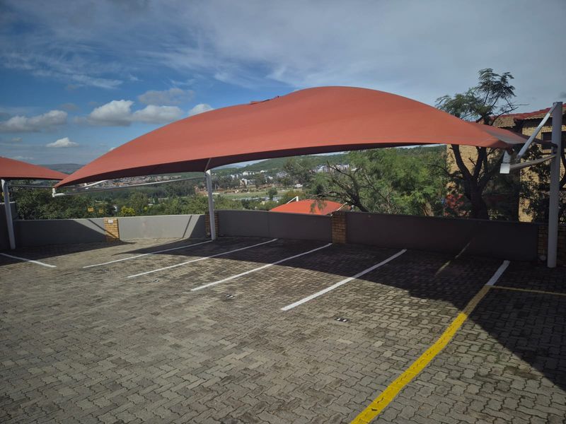 An outdoor parking area featuring a large shade cloth carport structure and clearly marked paved parking bays.
