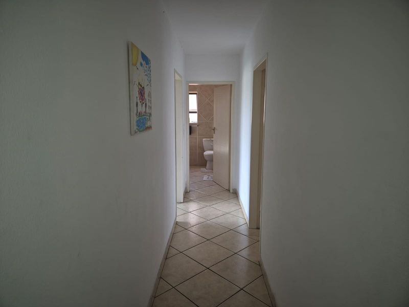 A simple interior hallway with tiled flooring, providing access to adjacent rooms including a bathroom.