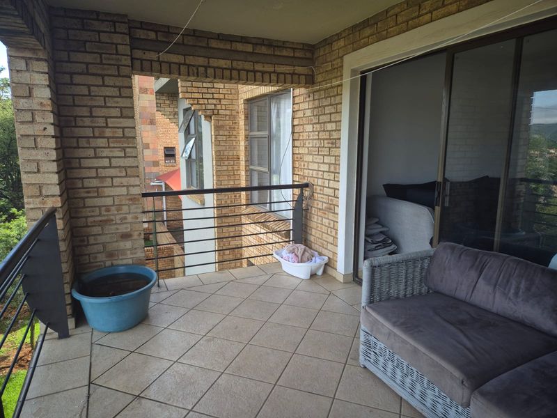 A covered balcony featuring brick walls, tiled flooring, and a metal railing, accessible via a large sliding glass door.