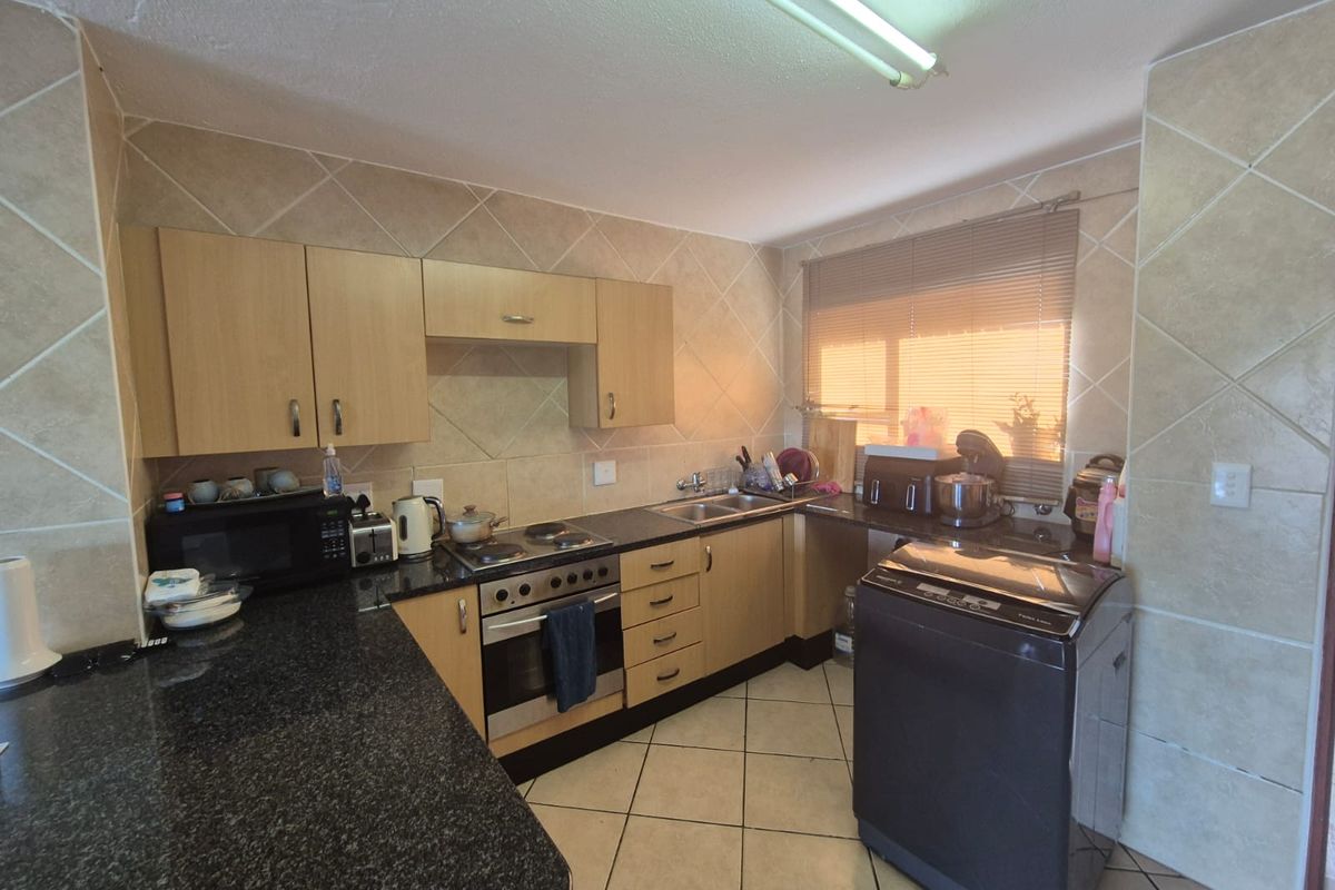 A functional kitchen featuring light wood cabinetry, dark granite countertops, a built-in oven with electric hob, and tiled finishes throughout.