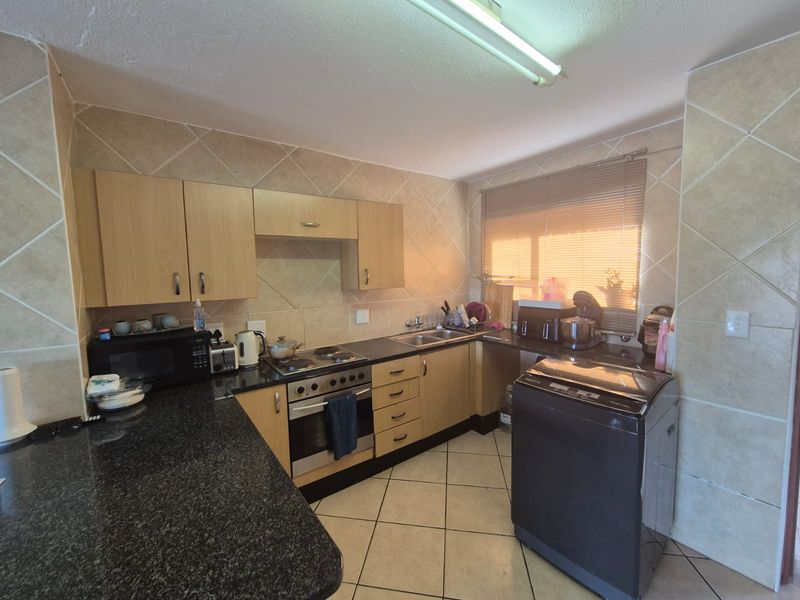 A functional kitchen featuring light wood cabinetry, dark granite countertops, a built-in oven with electric hob, and tiled finishes throughout.