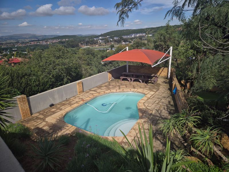 Outdoor pool area featuring stone paving, a brick boundary wall, and a shade sail, offering elevated views of the surrounding landscape.