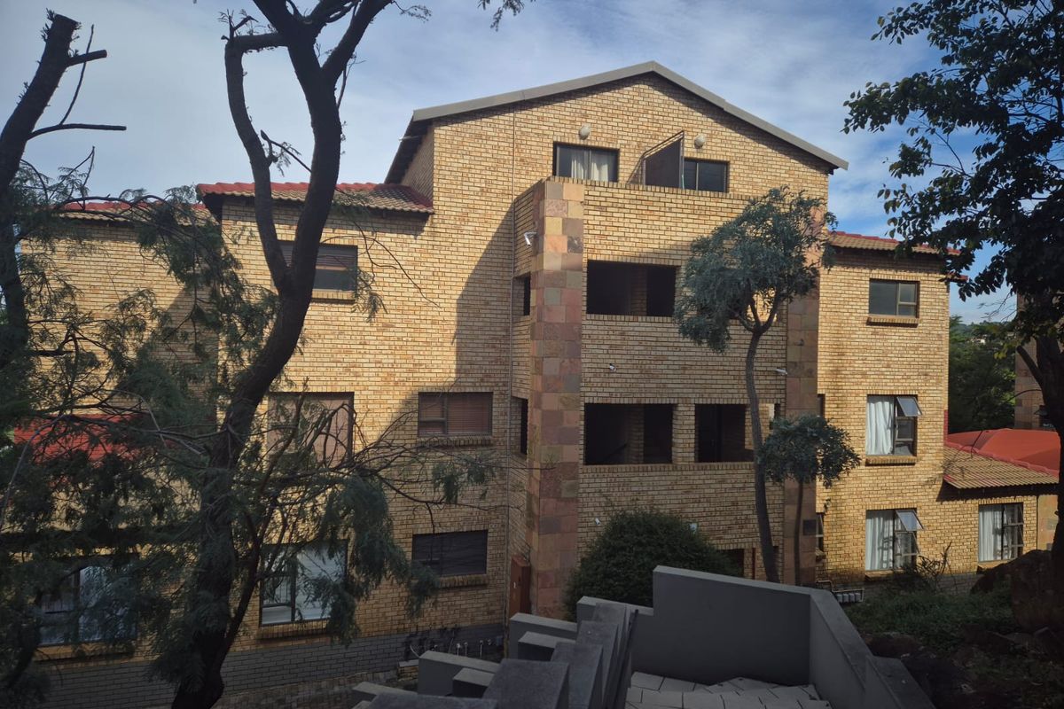 A multi-story apartment building featuring a face brick facade, tiled roof, and multiple balconies, viewed from an elevated outdoor position.