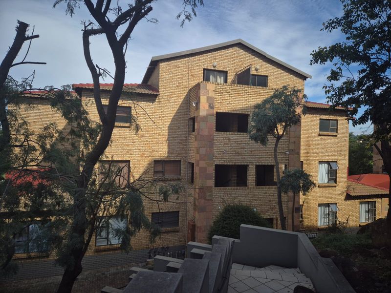 A multi-story apartment building featuring a face brick facade, tiled roof, and multiple balconies, viewed from an elevated outdoor position.