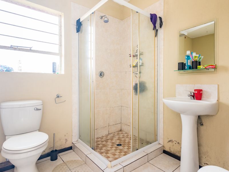 A functional bathroom featuring a shower enclosure, pedestal basin, and toilet, currently showing signs of wear and requiring cosmetic updates to the wall finishes.