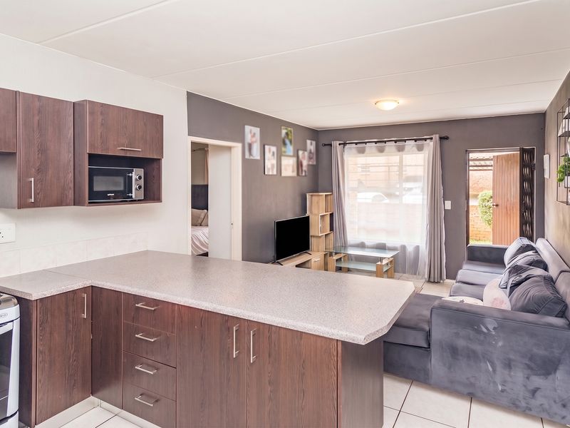 Open-plan living area featuring a functional kitchen with built-in cabinetry, oven, and hob, seamlessly flowing into a comfortable lounge space with direct outdoor access.