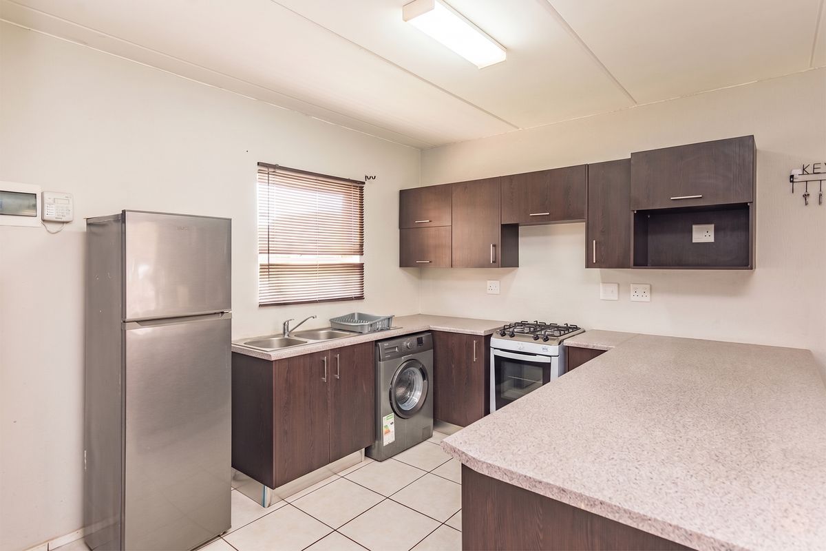 Functional kitchen featuring dark wood cabinetry, laminate countertops, a gas hob, built-in oven, and tiled flooring with space for laundry appliances.