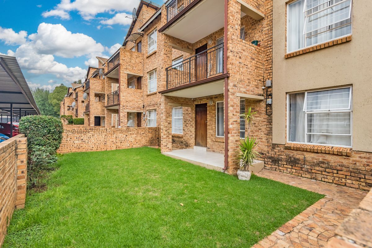 Rear view of a multi-story apartment complex featuring face brick construction, private balconies, and a shared ground-level garden area with paved walkways.