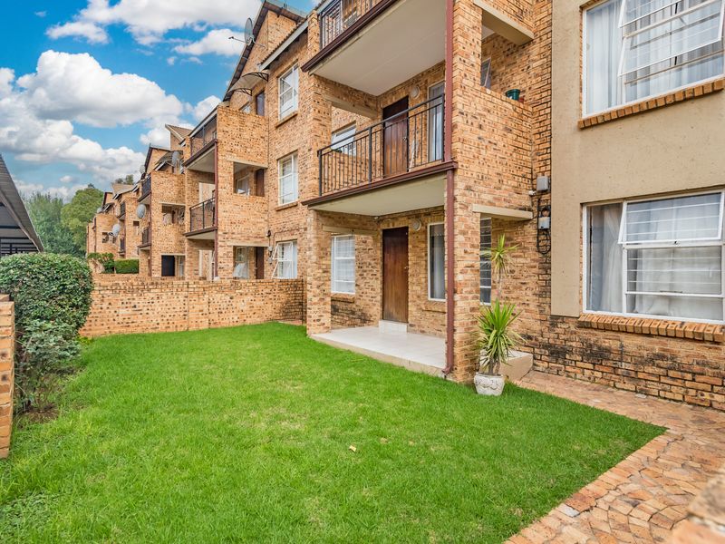 Rear view of a multi-story apartment complex featuring face brick construction, private balconies, and a shared ground-level garden area with paved walkways.