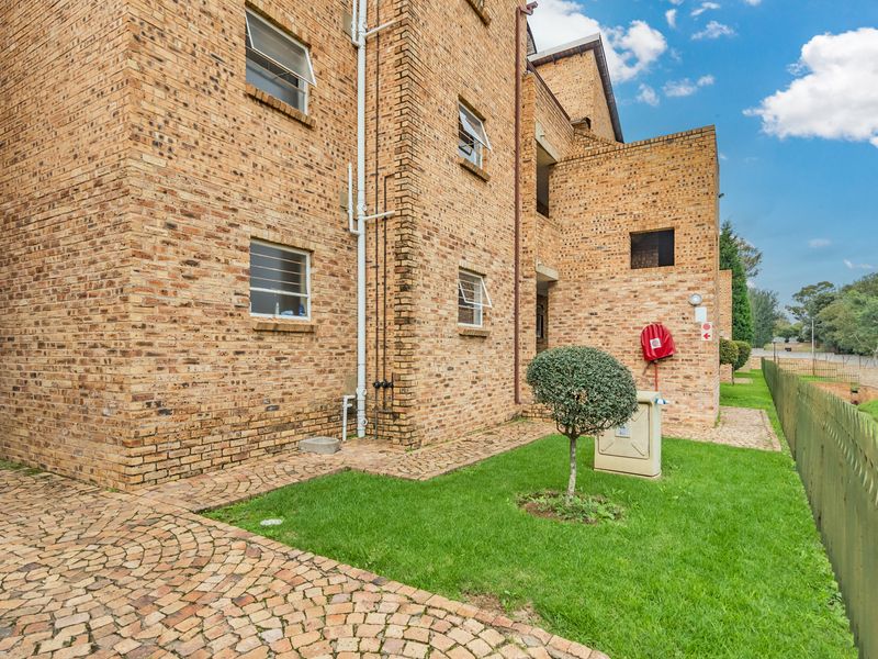 A view of the rear exterior of the apartment building featuring face brick construction, paved walkways, and well-maintained green space.