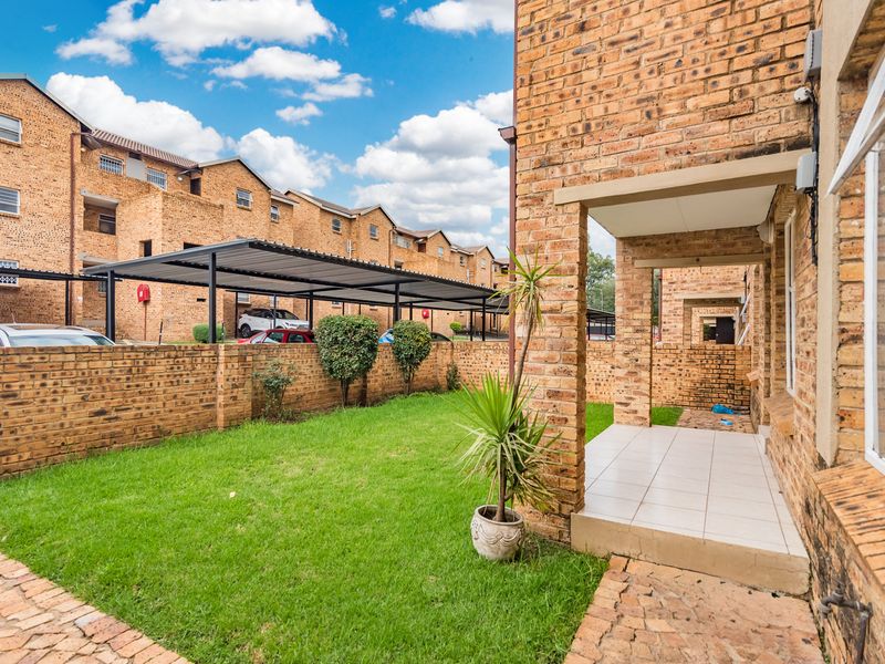A private rear garden featuring a tiled patio, established lawn, and face brick boundary wall, set within a well-maintained apartment complex.