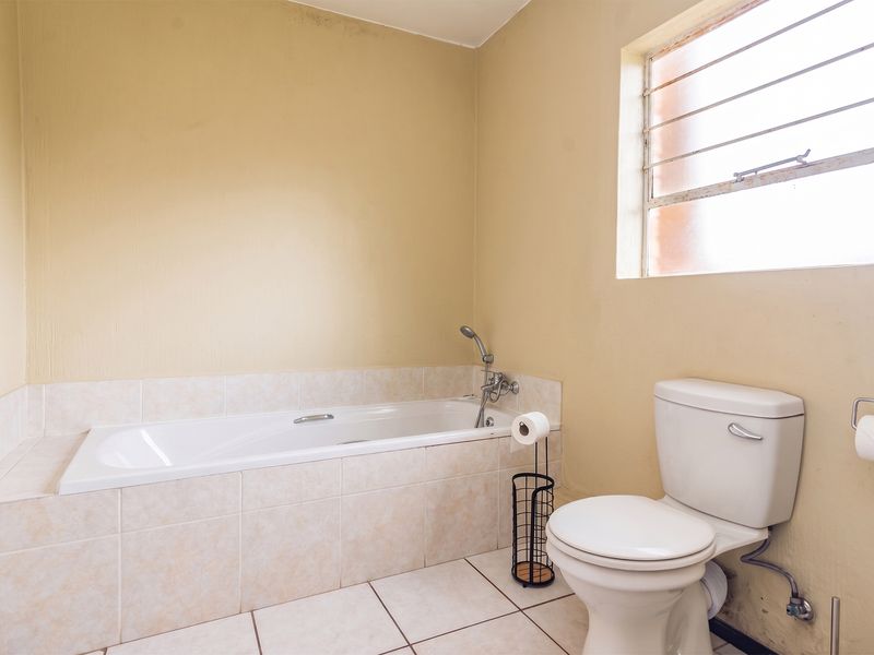 A functional bathroom featuring a built-in bathtub, standard toilet, and tiled finishes, requiring cosmetic updates to modernize the space.