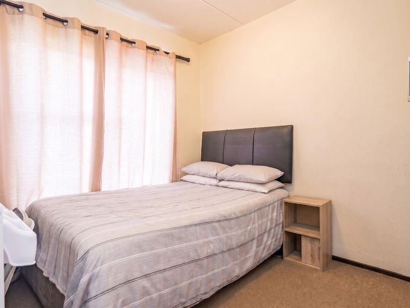 A functional bedroom featuring carpeted flooring and a window with installed curtain rods, providing a neutral base for personalization.