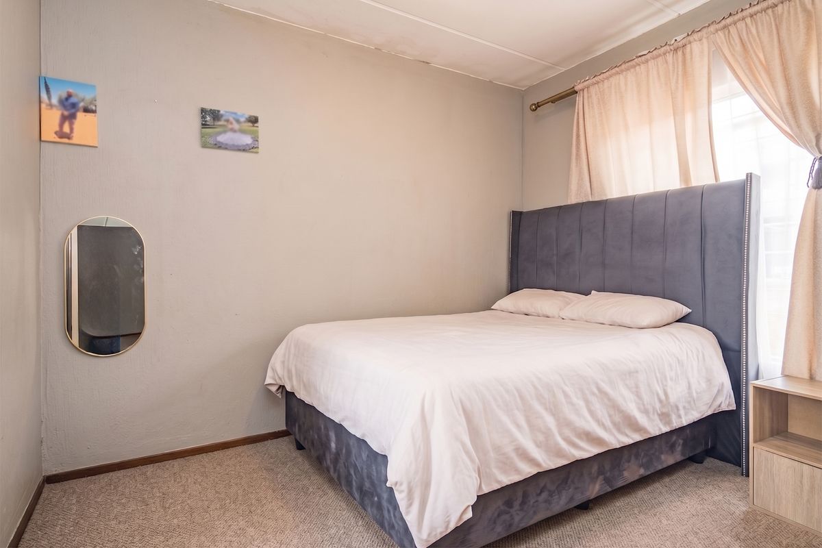 A bedroom featuring carpeted flooring and a window with curtain rod, showing signs of wear on the ceiling.