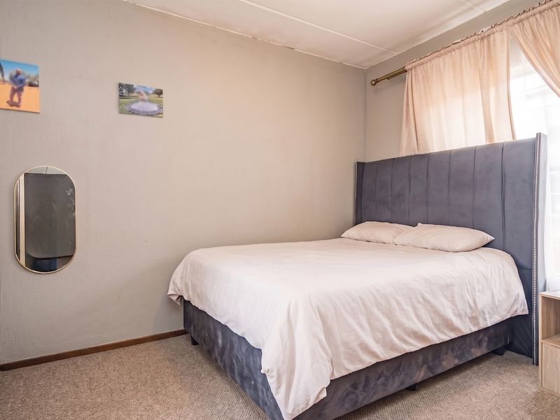 A bedroom featuring carpeted flooring and a window with curtain rod, showing signs of wear on the ceiling.