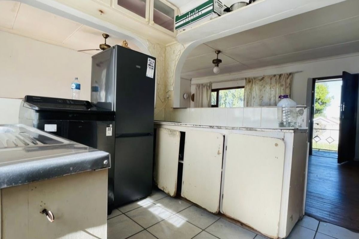 A dated kitchen featuring original cabinetry, tiled flooring, and an open-plan layout leading to an exterior entrance.