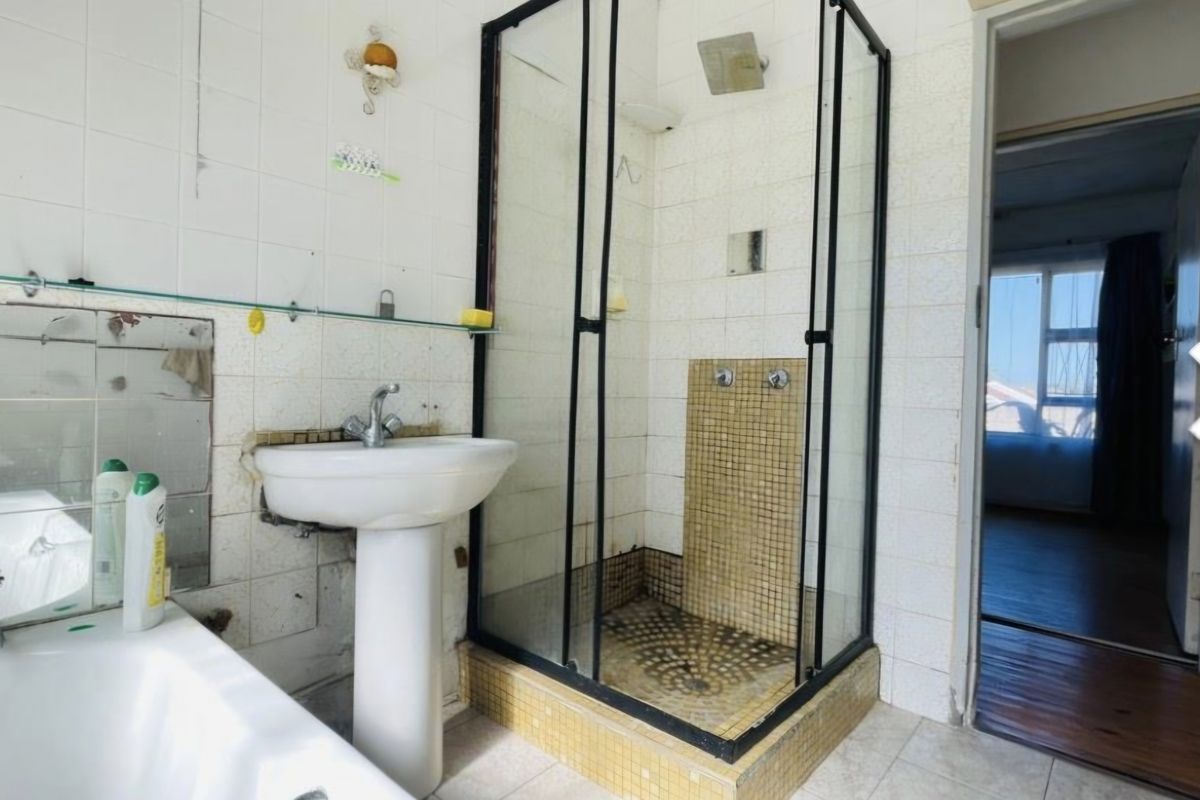 A dated bathroom featuring a pedestal basin, a separate shower enclosure with black framing, and a bathtub, requiring cosmetic updates to finishes.