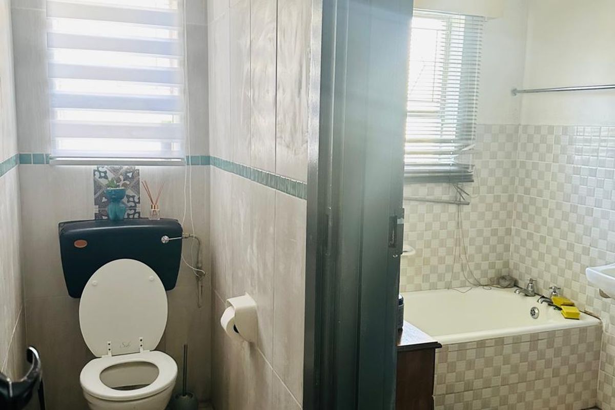 A functional bathroom featuring a separate toilet area, tiled walls, a bathtub, and a window for natural light.