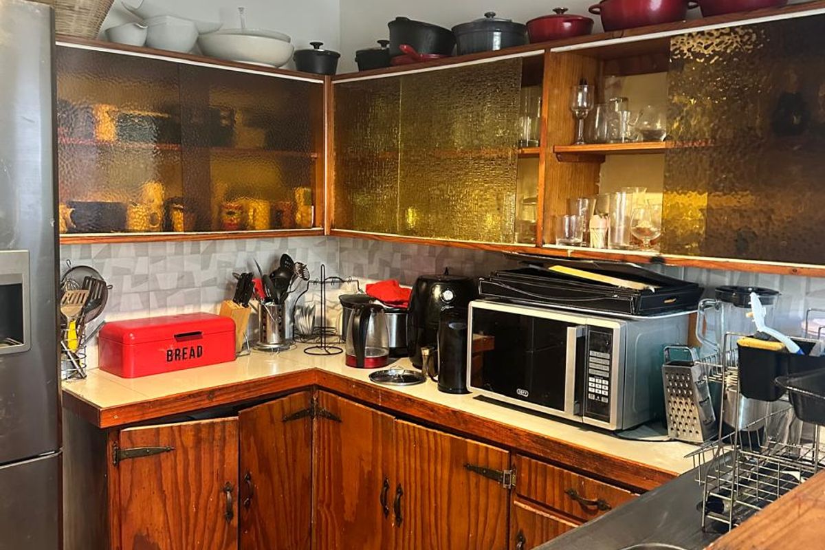 A dated kitchen featuring wood-grain cabinetry, textured glass upper cabinets, a stainless steel sink, and tiled flooring.