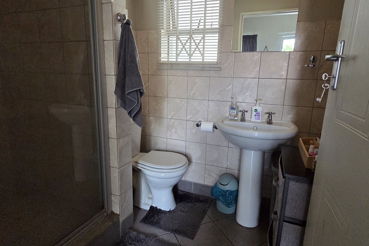 A functional bathroom featuring a pedestal basin, a toilet, and a glass-enclosed shower with neutral wall tiling and a window for natural light.