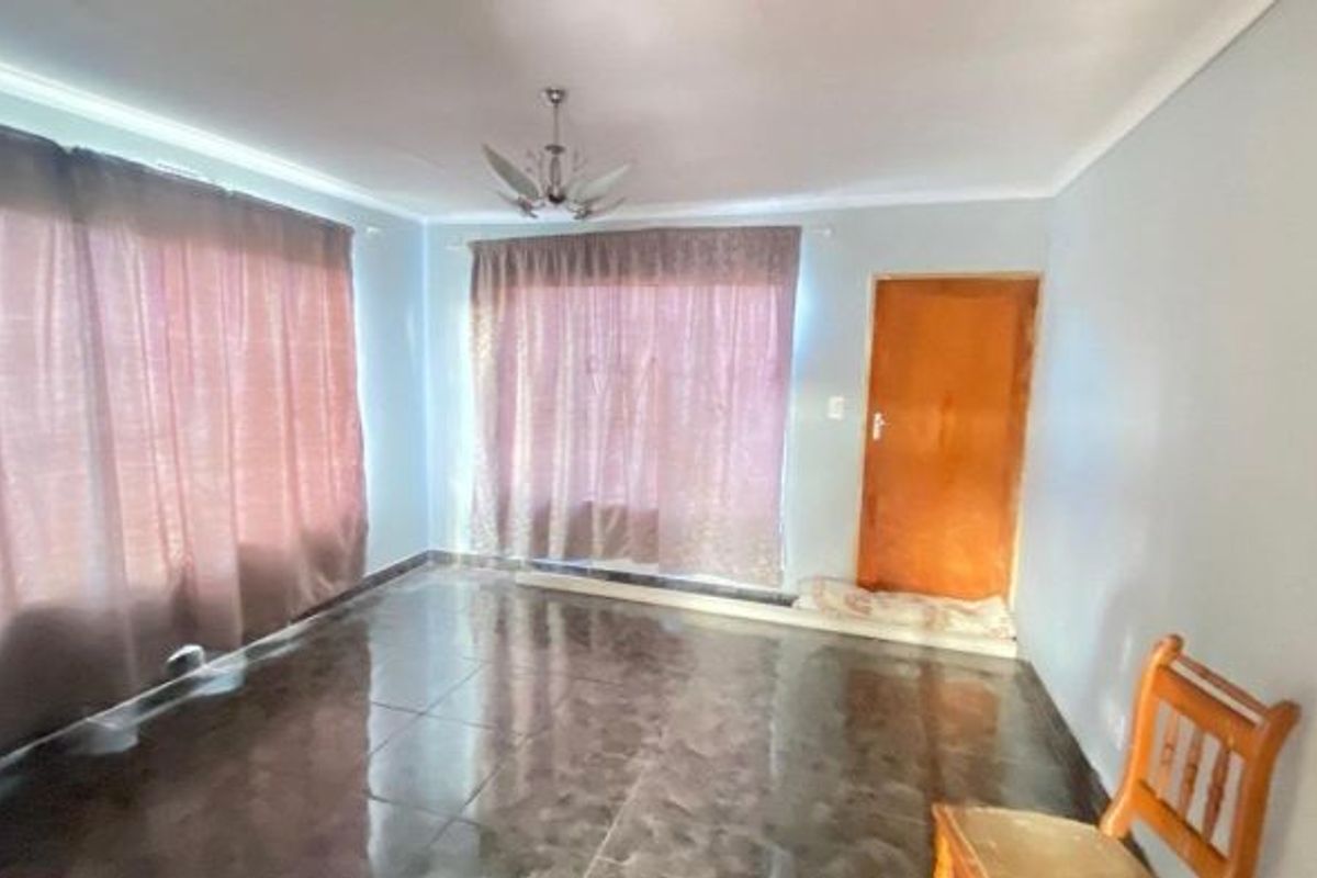 A spacious living room featuring large windows with curtains, tiled flooring, and a central ceiling light fixture.