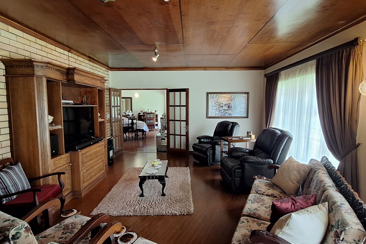 Spacious living room featuring a warm wood-paneled ceiling, brick accent wall, and classic french doors leading to an adjacent room.
