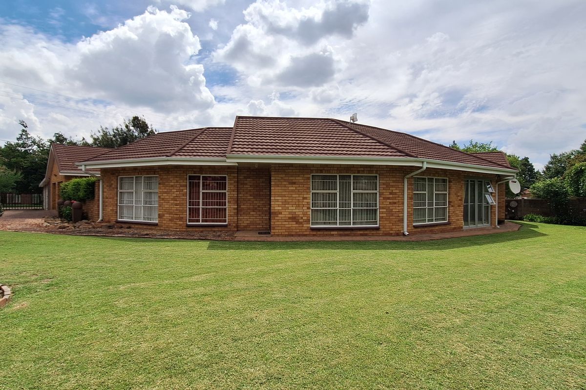 A well-maintained single-story brick house featuring a tiled roof, aluminium window frames with security bars, and a spacious surrounding lawn.