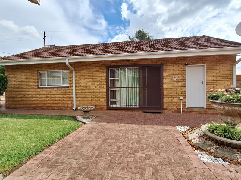 A well-maintained rear exterior view featuring a brick facade, tiled roof, paved patio area, and a neat lawn.