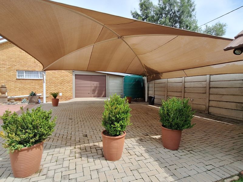 A paved outdoor area featuring a large shade sail, brick walling, and a water storage tank, providing a functional and shaded exterior space.
